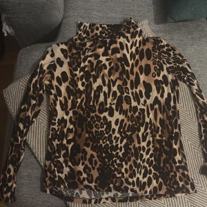Leopardmönstrad polotröja Laura Kent - Snygg polotröja från Laura Kent med leopardmönster i bruna och svarta toner. Tröjan har lång ärm och hög krage, perfekt för dig som vill sticka ut med ett djuriskt print. Materialet känns mjukt och följsamt mot huden.viscos👌