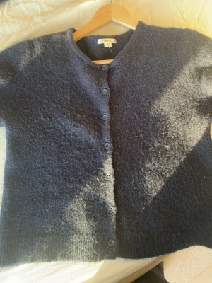 Mörkblå kofta från Gina Tricot - Säljer en mysig mörkblå kofta från Gina Tricot i storlek 158/164. Koftan är stickad med fluffig yta, har rund hals och knäpps med fem knappar framtill. Perfekt att slänga på sig när det är kyligt ute.