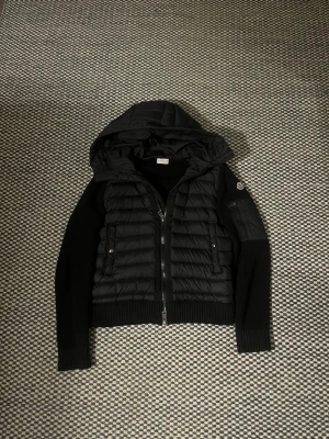 Svart moncler cardigan - Svart moncler cardigan, jag säljer denna jackan eftersom den har blivit för liten för mig. Den har en liten skada som jag sytt ihop men skadan blir inte värre. Kan droppa i pris vid snabb köp