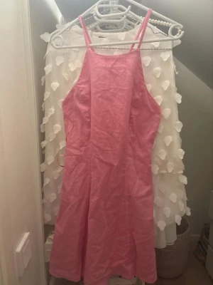 Rosa linnéklänning  - Säljer en snygg rosa klänning från ginatricot i storlek S. Klänningen är gjord i linne, har smala axelband som korsas i ryggen och en rak, kort siluett. Perfekt för varma dagar och har en fräsch, ljus rosa färg. Dragkedja i sidan för enkel påklädning.