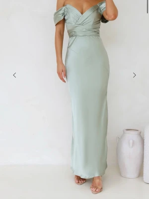 Balklänning  - Säljer en fin sage grön långklänning i satin material med offshoulder och omlottdetalj upptill. Klänningen har figurnära passform och dragkedja i ryggen. Perfekt för speciella tillfällen. Den har kommit till användning vid 1 tillfälle och har små slitage precis vid slutet av klänningen, men det är inget som märks