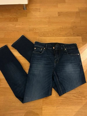 Mörkblå tapered jeans från Junk de Luxe - Snygga mörkblå jeans från Junk de Luxe med tapered fit och Superflex-material för extra komfort. Klassisk femficksdesign, med detaljerade sömmar och läderpatch bak i midjan. Jeansen har dragkedja och knappstängning samt subtila slitningar framtill. I storlek 31/34. Endast använda en gång