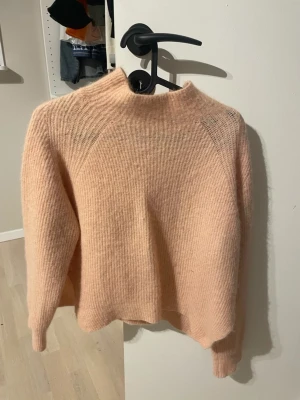 Ljusrosa stickad tröja By Malene Birger - Supermjuk och fluffig ljusrosa stickad tröja från By Malene Birger. Tröjan har en högre halsringning och långa ärmar, perfekt för kyliga dagar. Oversized passform som ger en avslappnad och trendig look.