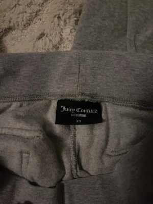 Grå mjukisbyxor Juicy Couture XS - Grå mjukisbyxor från Juicy Couture i storlek XS. Byxorna har en bred resår i midjan och snörning samt fickor på sidorna. Materialet är mjukt och bekvämt, perfekt för chill dagar. Diskret Juicy Couture-logga broderad på fickan.