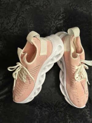 Ljusa rosa sneakers från Magza 39  - Säljer ett par snygga ljusrosa sneakers från Magza med vit chunky sula och vita snören. Ovandelen är stickad i syntetmaterial och har coola detaljer längs sidorna. Skorna har rund tå och platt sula, perfekt för dig som gillar sportig och trendig stil.
