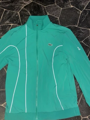 Grön lacoste windbreaker  - Snygg grön vindjacka från Lacoste  Som är köpt för 2000 utomlands har bara använt i typ 2 månader frf nytt skick inga skador ingeting 