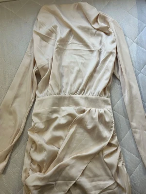 Bikbok - En super elegant silk klänning champagnefärgad klänning från Bik Bok - Säljer en stilren kort champagnefärgad klänning från Bik Bok i storlek M. Klänningen har lång ärm, markerad midja och är tillverkad i ett mjukt, slätt material som ger en elegant känsla. Passformen är normal och klänningen har en kort längd.