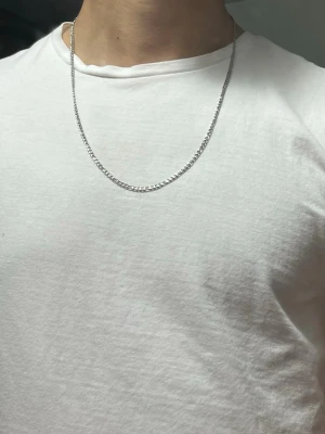 Kedja i silverfärgad metall 60 cm - Säljer en stilren silverfärgad kedja i metall, ca 60 cm lång. Kedjan har klassisk platt länkkedja och passar perfekt till en enkel t-shirt eller för att layera med andra smycken. Enkel karbinhake för smidig användning. Passar till allt!