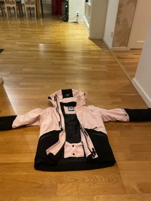 Rosa och svart vindjacka McKinley 146 - Säljer en snygg rosa och svart vindjacka från McKinley i storlek 146. Jackan har huva, dragkedja framtill, två fickor med dragkedja och coola svarta detaljer på ärmar och huva. Perfekt om man ska åka skidor, denna är använd en vecka. Mycket bra. Vid armen fins också en perfekt ficka för att lägga skid kort i💗