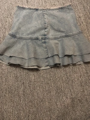 Ljusblå jeanskjol med volang, strl 32 - Säljer en ljusblå jeanskjol från Dual i storlek 32. Kjolen har en snygg volang nedtill och rå kant upptill, samt dragkedja bak. Perfekt för dig som gillar denim och vill ha en cool, feminin look. Passformen är normal och materialet är bomull. Helt oanvänd!! Priset kan diskuteras vid snabb affär 🌸