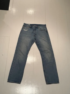Levi's 551z blå jeans straight fit -  blå Levi's 551z jeans med  straight fig och femficksmodell. Jeansen har en ljus tvätt och är tillverkade i slitstarkt bomullsjeans. Ikonisk läderpatch bak i midjan och knappgylf framtill. Perfekta för en avslappnad och tidlös stil.