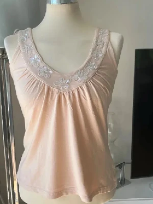 Beige linnetopp med paljettblommor - Supersöt beige linnetopp från Kaffe med v-ringning och blommiga paljettbroderier längs ringningen. Köpt secondhand men aldrig använt av mig, kontakta gärna vid frågor! 💕