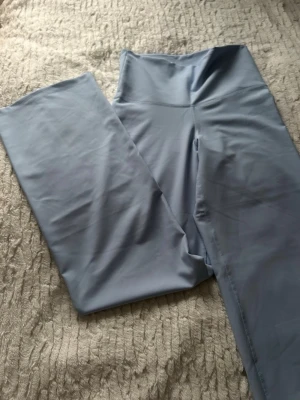 Ljusblå vida byxor med hög midja - Säljer ett par ljusblå byxor med hög midja och vida ben. Materialet känns mjukt och stretchigt, perfekt för en chill och trendig look. Passar dig som gillar stilrena och enkla plagg med en modern twist. Nya med pris lapp aldrig använda. 