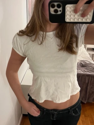 Vit croppad topp från Brandy Melville - Säljer en söt vit croppad topp från Brandy Melville. Toppen har korta ärmar, rund halsringning med vågig kant och är lätt ribbad i materialet. Passformen är normal och tyget är mjukt och stretchigt, perfekt till jeans eller kjol.