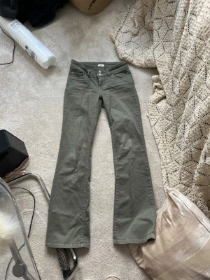Olivgröna bootcut byxor med nitar - Säljer ett par ljusgröna bootcut byxor med snygga sömar på bakfickorna. Byxorna har låg midja, klassisk femficksmodell och är gjorda i mjuk bomull. Perfekta för dig som vill ha en chill men ändå trendig look. Det är från butiken Nelly och knappt använda. Strl 36