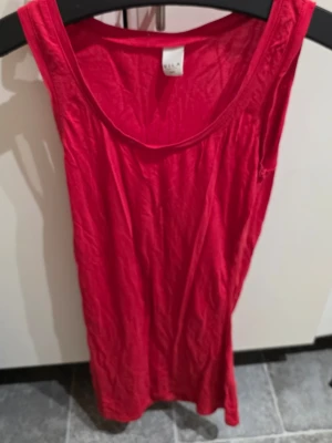 Röd linnetopp från Vila XS/S - Snygg röd linnetopp från Vila i storlek XS/S. Toppen är ärmlös med rund halsringning och har en enkel, rak passform. Materialet är mjukt och lätt, perfekt för varma dagar. Färgen är intensivt röd och toppen är stilren utan mönster eller extra detaljer.