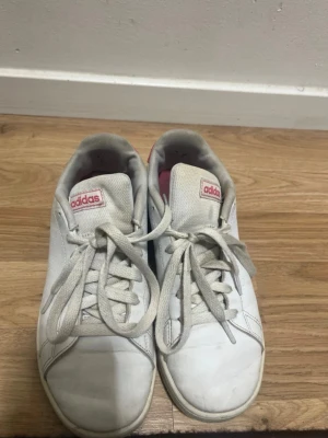 Adidas Advantage White Sneakers - Adidas Advantage sneakers in white with pink details. Classic and clean design – perfect for everyday wear, school, or casual outfits. • Brand: Adidas • Model: Advantage • Color: White with pink accents • Size: US 5 / UK 4.5 / EU 37⅓ / JP 235 • Condition: Used, good condition – normal signs of wear (see photos) • Material: Synthetic leather • Made in Indonesia Comfortable, lightweight, and easy to style with anything. From a smoke-free home. Feel free to message me if you have any questions 😊 