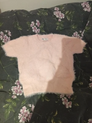Ljusrosa stickad tröja från Zara - Supermjuk och fluffig ljusrosa stickad tröja från Zara i storlek S. Tröjan har korta ärmar och rund hals, perfekt för dig som gillar en cozy och söt look. Materialet är stickat och har en lätt luddig yta som ger extra mysfaktor. Prislappen sitter kvar, och orginal priset är 259 kr 