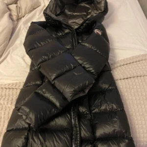Svart lång dunjacka från Colmar - Snygg svart dunjacka från Colmar med huva och lång passform. Jackan har quiltad design, dragkedja framtill och ett diskret Colmar-märke på ärmen. Perfekt för kalla dagar och har en stilren look som funkar till det mesta. Använd endast i 2 månader, jag betalade 6000kr nypris och kan tänka mig sälja den vid snabb affär för 3200kr. Storleken passar till 36 och även 38.