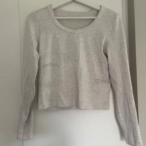 Ljusgrå långärmad basic tröja - En enkel och stilren ljusgrå långärmad tröja med rund halsringning. Perfekt att matcha med jeans eller kjol för en clean look. Mjuk och skön, passar året runt.