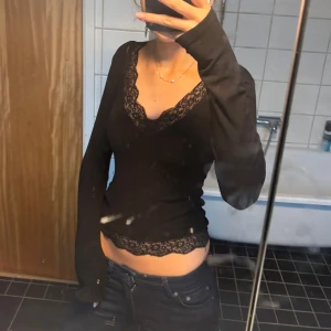Svart långärmad topp med spets - Svart långärmad topp med v-ringning och fina spetsdetaljer längs halsringning och nederkant. Säljer då jag inte får användning för längre. Pris går att diskuteras