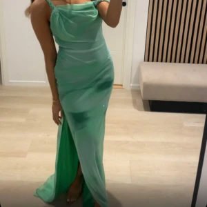 Grön långklänning med slits - Snygg grön långklänning med smala axelband och draperad överdel. Klänningen har en elegant slits framtill och figurnära passform som framhäver siluetten. Perfekt för dig som vill sticka ut med en fräsch färg och stilren look.