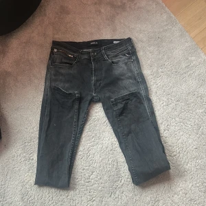 Svarta Replay jeans med slitningar - Snygga svarta jeans från Replay med diskreta slitningar och tvättad look. Klassisk femficksmodell med dragkedja och knapp framtill. Jeansen har raka ben och tydliga sömmar på bakfickorna. Perfekta för en avslappnad och cool stil.