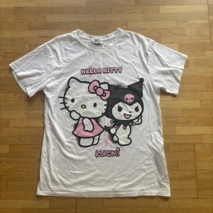 Hello Kitty x Kuromi t-shirt från New Yorker - Vit loose fit t-shirt från New Yorker med stort Hello Kitty och Kuromi-tryck framtill i svart och rosa. Klassisk rund hals och korta ärmar. Perfekt för dig som älskar kawaii och vill ha en chill och söt stil.