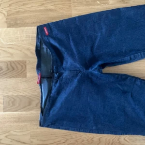 Mörkblå bootcut jeansbyxor - Snygga mörkblå jeansbyxor med bootcut passform och låg midja. Byxorna har en klassisk look utan synliga fickor eller knappar framtill och är tillverkade i ett stretchigt jeansmaterial. Perfekta för dig som gillar retrovibbar och vill ha ett par byxor med utsvängda ben.