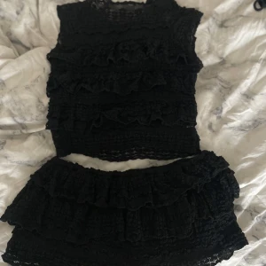 Svart volangkjol med en topp  - Supersöt svart kortkjol med flera lager volanger och smockad struktur. Kjolen har en trendig och lekfull look som passar perfekt till crop tops eller stickade tröjor. Materialet känns mjukt och följsamt mot huden.