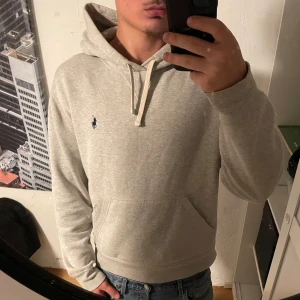 Grå hoodie från Polo Ralph Lauren - Snygg ljusgrå hoodie från Polo Ralph Lauren med klassisk broderad logga på bröstet. Tröjan har huva med snörning, känguruficka och är tillverkad i mjuk bomullsmix. Perfekt för chill dagar eller när du vill ha en clean look. Kom med bud eller frågor, fraktar snabbt! Perfekt skick, storlek M.
