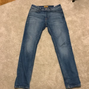 Blå tapered jeans från Jack & Jones - Säljer ett par blå jeans från Jack & Jones, modell Tapered/Mike. Storlek 30/32. Jeansen har klassisk femficksdesign, normal midja och avsmalnande ben. Tillverkade i mjukt denimtyg med snygga slitningar framtill. Perfekta för en avslappnad och trendig look. 