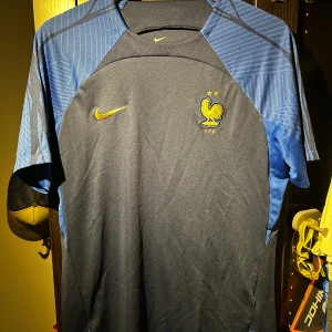 Frankrike Nike fotbollströja blå L - Säljer en Frankrike fotbollströja från Nike i slim fit, storlek L. Tröjan är mörkblå med ljusblå detaljer och har korta ärmar. Materialet är lätt och andas, Dri-Fit. Guldig Nike-logga och Frankrikes emblem