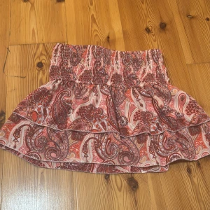 Mönstrad kortkjol från SHEIN - Supersöt kortkjol från SHEIN i storlek S med mönster i rödbruna och beige toner. Kjolen har smock i midjan och volangkant nertill, vilket ger en skön och avslappnad vibe. Perfekt för dig som gillar färg och mönster! 🌷