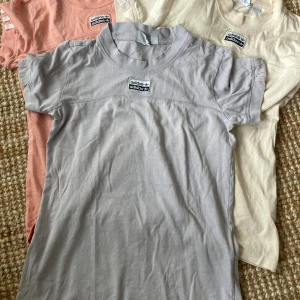3x Adidas t-shirt med broderad logga - Säljer en snygg Adidas t-shirt i ljusgrått med broderad och tryckt logga framtill. T-shirten har korta ärmar, rund hals och är gjord i mjuk bomull. Perfekt för dig som gillar sportig stil och vill ha något bekvämt och trendigt.