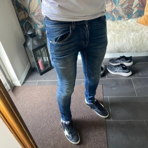 Tiger Of Sweden Jeans - Säljer ett par blå skinny jeans från Tiger Of Sweden i modellen Evolve. Jeansen har en tight passform, klassisk femficksdesign och snygga slitningar framtill. Tillverkade i Italien och gjorda i jeansmaterial. Perfekta för dig som gillar en smal siluett.