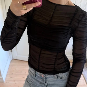 Svart mesh topp från H&M - Säljer en svart mesh topp från Divided i storlek XS. Toppen är långärmad, tight och har ett transparent, rynkat tyg som ger en cool och edgy look. Har en topp under så toppen är helt i mest och inget ”täckande” tyg