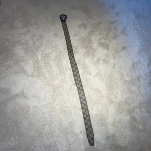 Gucci GG Supreme bälte med silverdetalj - Snyggt Gucci-bälte i klassiskt GG Supreme-mönster med beige och bruna toner. Bältet har en rund, silverfärgad spänne med GG-logga och är gjort i skinn med canvas-yttersida. Perfekt för att lyfta vilken outfit som helst med en lyxig touch.