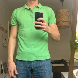 Gant - Fräsch grön pikétröja från GANT med klassisk krage och två knappar vid halsen. Tröjan har korta ärmar och diskret broderad logga på bröstet. 