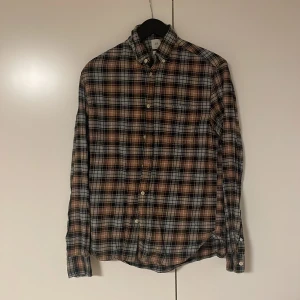 Rutig skjorta från H&M L.O.G.G. brun/svart - Säljer en rutig skjorta från H&M L.O.G.G. i bruna, svarta och grå toner. Skjortan har klassisk krage, knäppning framtill och en bröstficka. Regular fit och långärmad, perfekt för en avslappnad stil. Materialet är mjuk bomull.