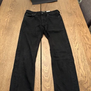 Svarta tapered jeans Jack & Jones - Svarta jeans från Jack & Jones med tapered fit, modell Mike. Jeansen har en stilren look som funkar till det mesta. Perfekta om du gillar en smalare passform utan att de sitter helt tight. W28 L30