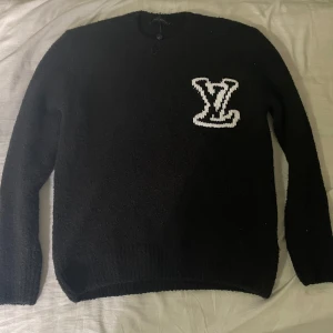 Svart stickad tröja Louis Vuitton XS - Säljer en svart stickad tröja från Louis Vuitton i storlek XS men passar M också. Tröjan har ett stort vitt LV-logo broderat på bröstet och är långärmad med rund hals. Materialet känns riktigt lyxigt och mjukt. Perfekt för dig som vill ha något stilrent men ändå sticker ut.