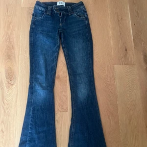 Blå bootcut jeans från BDG - Snygga mörkblå bootcut jeans från BDG med klassisk femficksdesign och dubbla knappar i midjan. Jeansen har en markerad utsvängd passform nertill och är tillverkade i ett robust denimtyg med snygga slitningar. Perfekta för dig som gillar retrovibbar och cool stil.