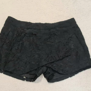Svarta spets-shorts från Amisu - Snygga svarta shorts från Amisu i storlek 42, täckta med blommig spets och med ett mjukt innerfoder. De har en rak och lite loose passform med midwaist. Perfekta för dig som vill ha en cool och feminin vibe på sommaren.