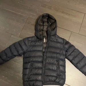 Svart dunjacka från Colmar med huva - Säljer en svart dunjacka från Colmar med huva och dragkedja. Jackan är quiltad och har två fickor med dragkedja framtill samt Colmar-logga på ärmen. Perfekt för kalla dagar och riktigt skön att bära. Perfekt vinterjacka 