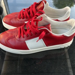 Valentino Garavani röda sneakers - Snygga röda och vita sneakers från Valentino Garavani med ikoniska nitar runt sulan. Skorna är i skinn med röda snören och har en cool kontrast mellan färgerna. Perfekta för dig som vill sticka ut med en lyxig streetstyle-look. box ingår ej.  nästan helt nya använda 3 gånger extremt populära skor och tillverkning finns ej kvar