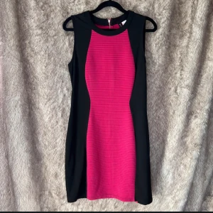 Svart och ceriserosa klänning H&M Divided - Snygg klänning med en ribbad cerise front. Klänningen har en figurnära passform och dragkedja bak. Den är jättefin.  Bredd 44 cm armhåla till armhåla Längd 88 cm