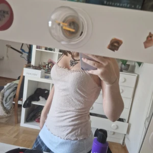 Beige blommig linnetopp från Intimissimi - Supersöt beige linnetopp från Intimissimi med små vita blommor och spetsdetaljer längs kanterna. Tunt och mjukt material med smala axelband och figurnära passform. Perfekt för varma dagar eller som lager under en skjorta.