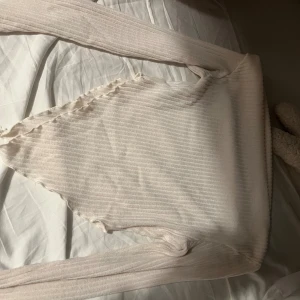 Ljusbeige ribbad omlottopp - Supersnygg ljusbeige omlottopp med långa ärmar och ribbad struktur. Toppen har en unik omlott-design med spetsiga kanter och är tillverkad i ett mjukt, stretchigt material som sitter skönt på kroppen. Perfekt för dig som gillar trendiga och stilrena plagg.