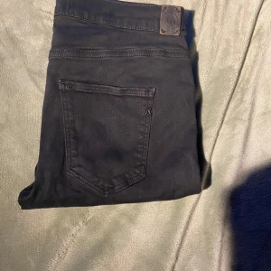 Svarta Replay Hyperflex jeans - Säljer ett par svarta Replay Hyperflex jeans i modellen Stella. Jeansen har klassisk femficksdesign, stretchigt material och normal passform. Perfekta om du vill ha ett par stilrena och bekväma jeans med snygg look. Passar till allt och är riktigt sköna på.